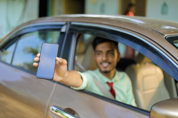 Young indian business man or employee sitting in car and showing mobile screen