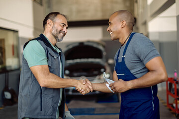 Happy mechanic greeting with his African American coworker at auto repair shop.