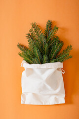 Christmas composition. Eco-bag with Christmas tree branches on an orange background. Christmas arrival and gift delivery concept. Top view, copy space.