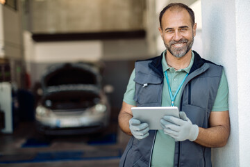 Happy auto mechanic using digital tablet in a workshop and looking at camera.