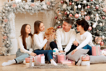 Happy family at home near a Christmas decorated tree with a dog and gifts, celebrating the new year.
