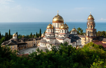 Fototapeta na wymiar Graceful, beautiful and sunny Male Simon the Conanite monastery with golden domes against the backdrop of the endless blue sea. New Byzantine style 1875. New Athos, Abkhazia.