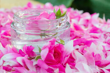 Facial gel in a transparent glass jar with flowers and rose petals.