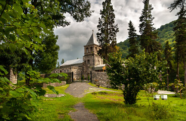 Fototapeta na wymiar A temple on a hill of yellow stone, surrounded by forest and green wooded mountains. Thunderous cloudy sky. Monastery of St. John Chrysostom, and his burial place in 407. Kamany, Abkhazia.