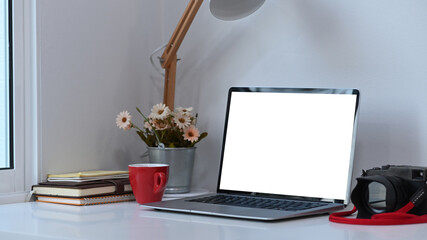 Photographer or designer work space with white blank screen laptop and equipment on white desk.
