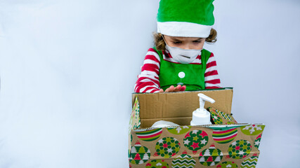 Little elf holding a COVID 19 pandemic present with a sanitizer, medical mask, and toilet paper. Conceptual photo of a gift during corona virus.