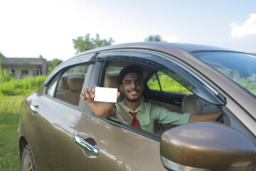 Young indian businessman or employee sitting in car and showing card
