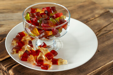 Chewing marmalade bottles of cola and bears on white plate on wooden background.