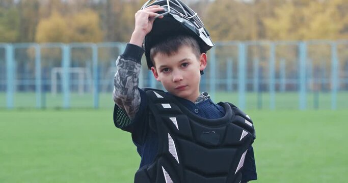 Portrait of a boy baseball player on a blurry background, the catcher puts on a protective helmet and looks at the camera, a serious look, 4k Slow Motion.