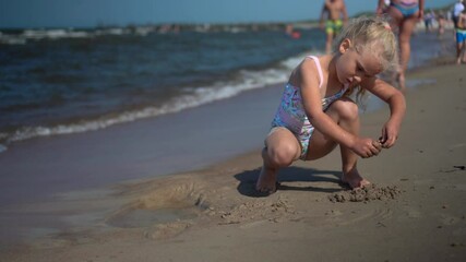 Preschooler girl dig hole in sand. Female child in swimsuit enjoy sea waves
