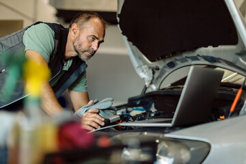 Mid adult mechanic running car diagnostic on laptop in auto repair shop.