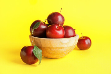 Bowl with fresh ripe plums on color background