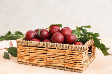 Wicker basket with ripe plums on light background