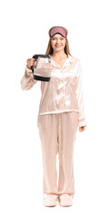 Young woman in pajamas holding electric kettle on white background