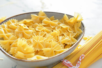 Bowl with uncooked pasta on light background