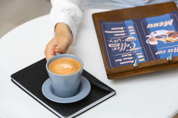 Woman with menu and cup of hot coffee in cafe