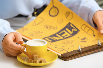 Woman with menu and cup of hot coffee in cafe