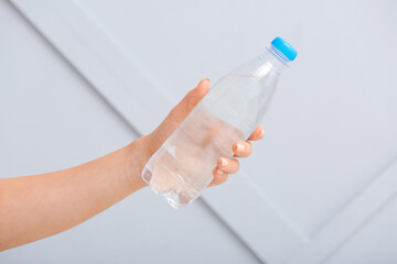 Female hand and bottle of water on light background