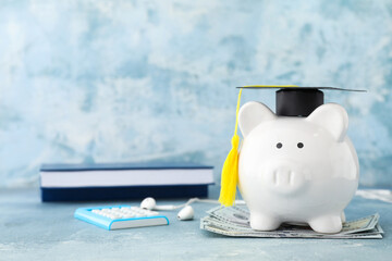 Piggy bank with graduation hat and money on table - obrazy, fototapety, plakaty
