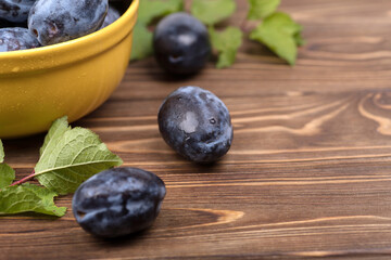 Lots of ripe juicy plums in a orange bowl on the wooden table.