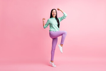 Full length photo of adorable lucky young lady wear teal pullover rising arms hands fists standing one leg isolated pink color background
