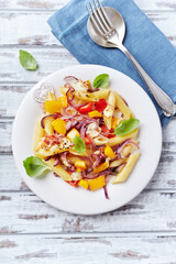 Penne pasta baked with peppers, red onion and mozzarella. Bright wooden background. Top view.	