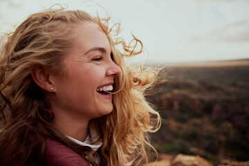 Closeup of a laughing young woman enjoying windy breeze touching face with hair flying while...