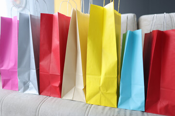 Many multi-colored paper bags with purchases standing on the sofa at home