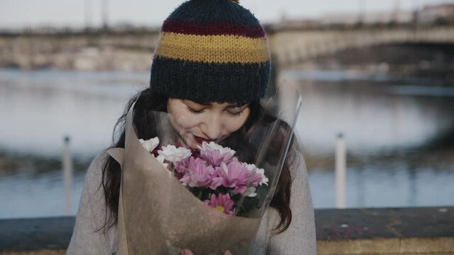 Portrait of beautiful asian girl walking with bouquet of flowers. Close-up happy woman holding bunch of flowers in hands outdoors. Romantic lady walking on street with flower bouquet after date.