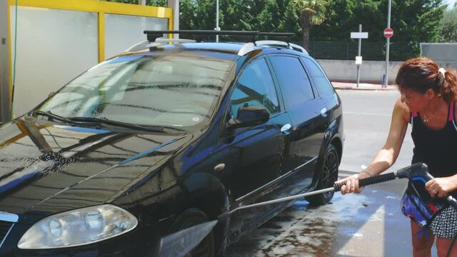 young caucasian woman rinsing and spraying her car clean at self service car wash