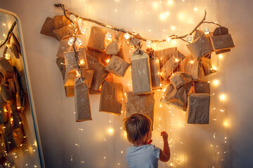 Caucasian Child Toddler with Magic Homemade Advent calendar on a tree branch on the wall of the...