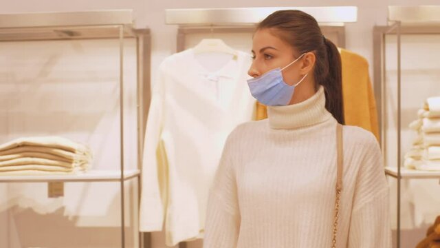 Young woman with long hair in ponytail walks near brown and white pullovers of new winter collection in department store. Concept leisure