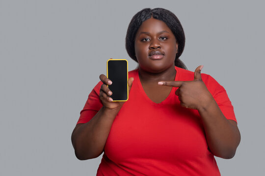 Young Dark-skinned Woman In Red Tshirt Holding A Smartphone