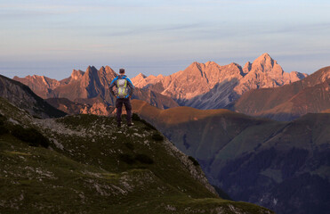 Hiker Man standing at amazing view from high mountain to many other peaks at Sunset. Allgau, Bavaria, Alps, Germany.