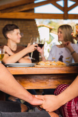 Portrait of a romantic and charming couple sitting at the table having a meeting with friends holding hands under the table.