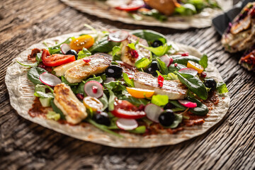 Open top vegetarian tortilla with salad, raddish, chery tomatoes, olives, pomegranate and grilled haloumi cheese