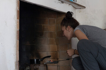 Fototapeta na wymiar woman squatting by the fireplace preparing the coals for cooking