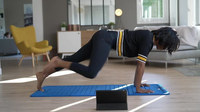 African-american woman doing virtual fitness exercices, digital class on tablet