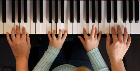 Mom and daughter play the piano in four hands. Top view