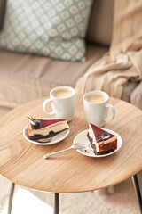 Fototapeta na wymiar food, junk-food, culinary, baking and holidays concept - pieces of delicious cake on saucers with spoons and coffee cups on wooden table