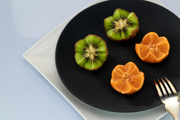 Fresh kiwi fruit and tangerines are on a black plate.Light background