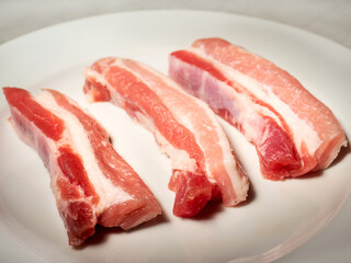 Fresh raw pork belly slices on a white plate. Meat industry product