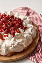 food, culinary, baking and cooking concept - close up of pavlova meringue cake decorated with red berries on wooden serving board and kitchen towel