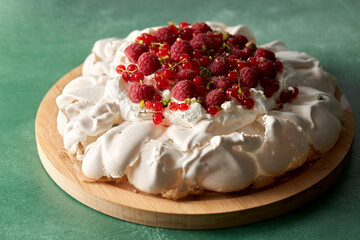 food, culinary, baking and cooking concept - close up of pavlova meringue cake decorated with red berries on wooden serving board