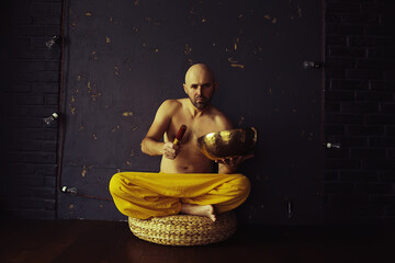 Tibetan singing bowl, a monk in yellow pants meditates and plays the musical bowl, Buddhism,...