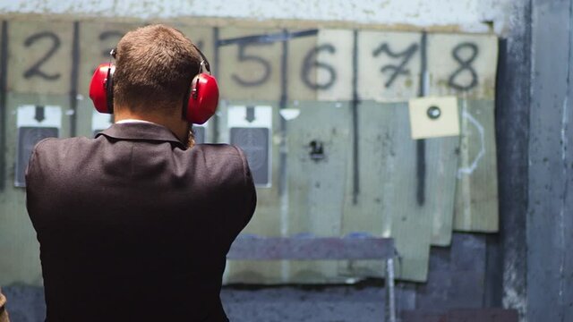 Man in suit shooting with gun at target in shooting range. Businessman takes lessons in shooting with a handgun