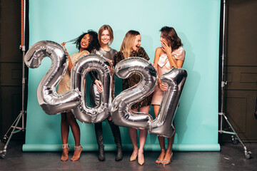 Beautiful Women Celebrating New Year.Happy Gorgeous Female In Stylish Sexy Party Dresses Holding Silver 2021 Balloons, Having Fun At New Year's Eve Party. Holiday Celebration.Charming Models