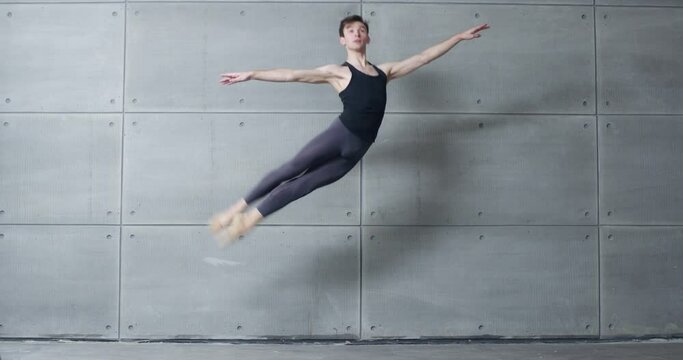 Male ballet dancer performs acrobatic elements of a ballet dance on a gray background, 4k slow motion.