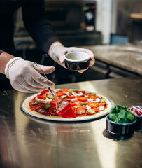 Chef in the pizzeria prepares a pizza and tastes it with olive oil.