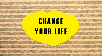 Yellow torn paper with the text CHANGE YOUR LIFE on a gray-pink background.